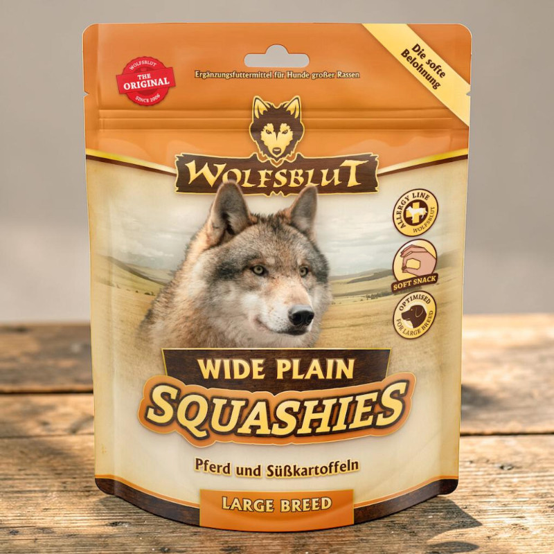 Emballage brun-beige vertical des Squashies « Wolfsblut » pour grandes races. Au centre, tête de loup réaliste sur steppe brun clair. Accent sur cheval et patates douces, friandise moelleuse. Symboles : sans céréales.