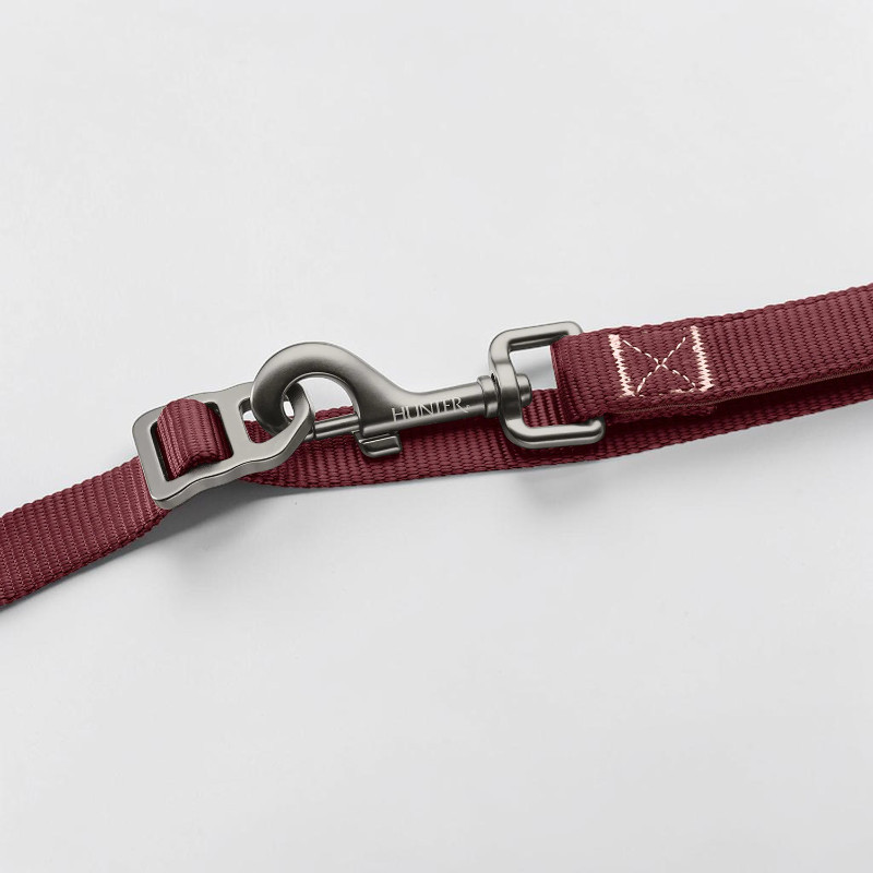 Laisse « Action » Hunter baie : nylon tissé rouge foncé, mousqueton de sécurité en aluminium gris foncé mat (logo Hunter gravé) et réglage de longueur. Coutures en X robustes pour résistance et visibilité réfléchissante.