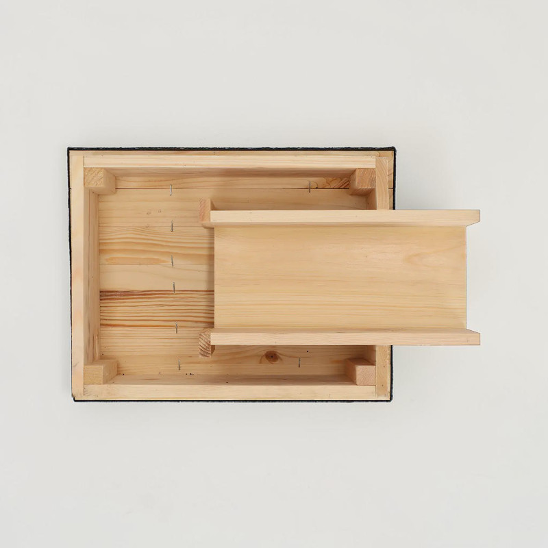 Face inférieure (intérieur ouvert) de la maisonnette pour hérissons L Esschert en épicéa clair visible. Construction robuste avec panneaux de fond et angles renforcés. Entrée tunnel allongée pour accès protégé. Bordure bitume.