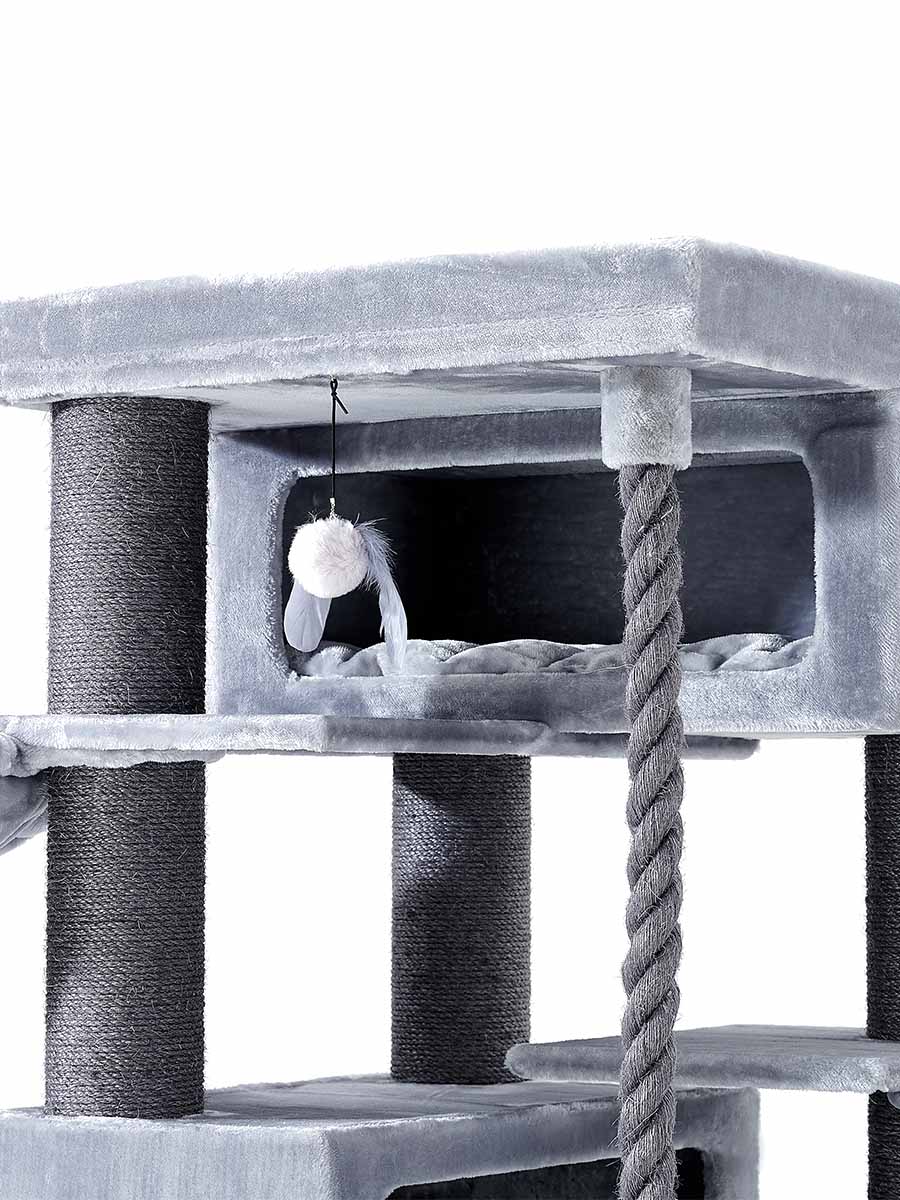 Light grey cat scratching post with multiple levels in soft plush. Dark grey posts are wrapped in sisal rope. A sleeping area with a soft mat is inside a cave. Feather toys hang from the top, with an integrated climbing rope.