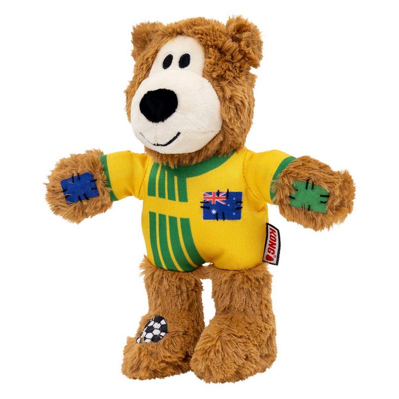 Brauner Plüschbär im gelb-grünen Sportoutfit wie ein Fußballtrikot, mit Aufnäher der australischen Flagge auf der Brust. Zottelige Pfoten mit blauen und grünen Flicken; ein Fuß mit Fußballmuster. Schwarze Augen, Nase, freundliches Lächeln.