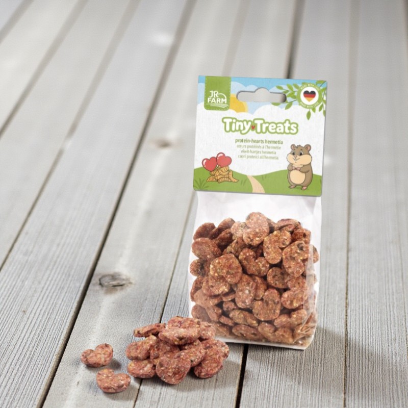 Verpackung Tiny Treats Protein Hearts mit herzförmigen Snacks auf hellem Holzgrund.