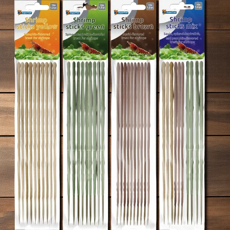 Vier Packungen SuperFish Garnelen-Sticks: Gelb, Grün, Braun und Mix, liegend auf Holz.