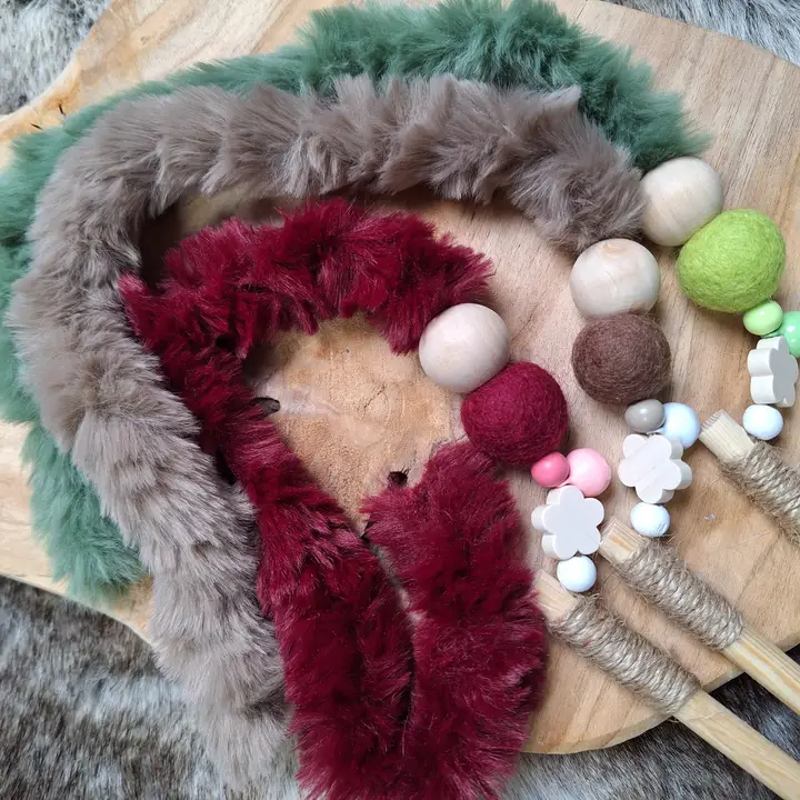 Drei farbige, fellartige Bänder und Holzspielzeug auf einem Holzbrett. Bänder in Grün, Grau und Rot. Holzperlen in verschiedenen Farben und Formen.
