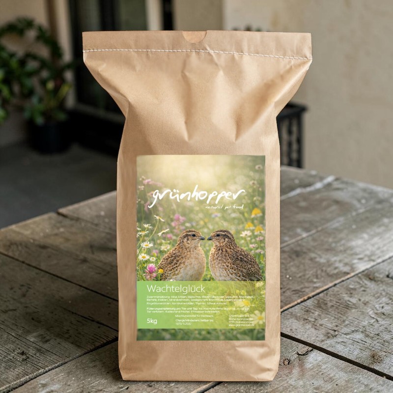 Brauner Papiersack mit dem Etikett „grünhopper natural pet food Wachtelglück“ auf einem Holztisch. Das Etikett zeigt zwei braun gesprenkelte Wachteln in einem Blumenfeld mit Margeriten und lila Blüten. Unten links: 5kg.