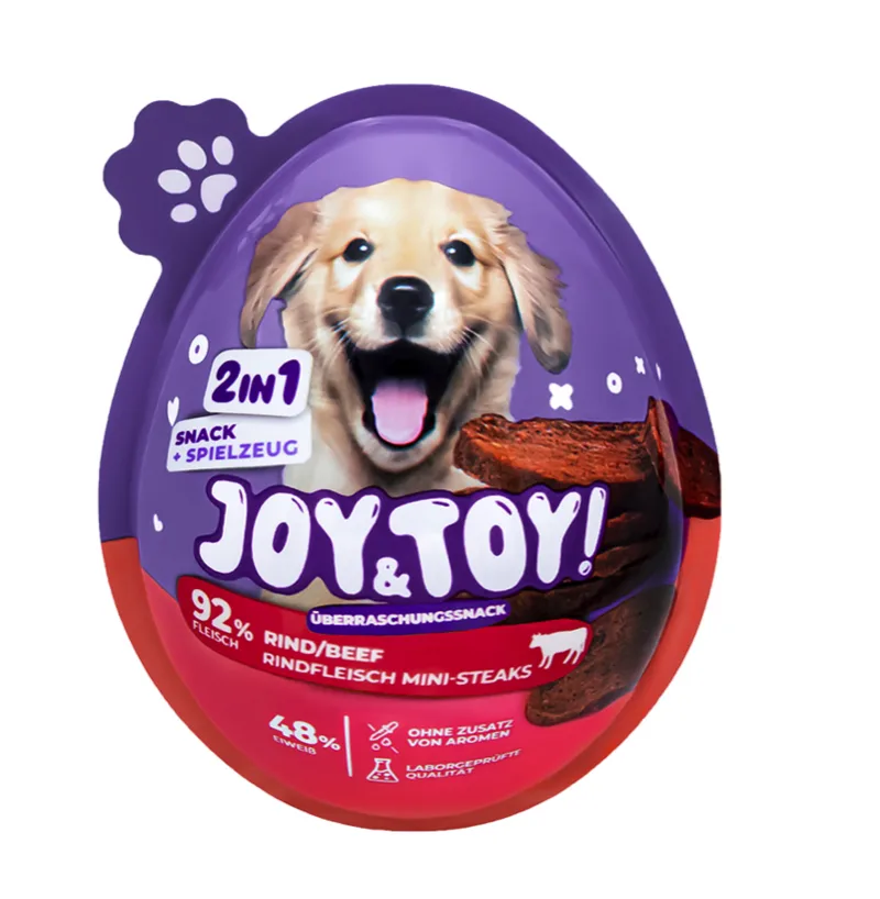 Lila-rote, eiförmige Verpackung für Hundeleckerlis. Oben ein fröhlicher, hellbrauner Welpe mit offenem Maul und herausgestreckter Zunge. Darunter Rindfleisch-Mini-Steaks, „JOY & TOY!“, „2 in 1 Snack + Spielzeug“, 92% Fleisch, laborgeprüft.