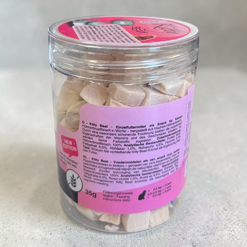 Transparent cylindrical container containing light beige, cube-shaped freeze-dried chicken snacks for cats. Pink sleeve featuring ‘Kitty Beat’, ‘chicken breast’ and ‘35g’, pink lid with logo. The snacks are uniformly shaped and visible.