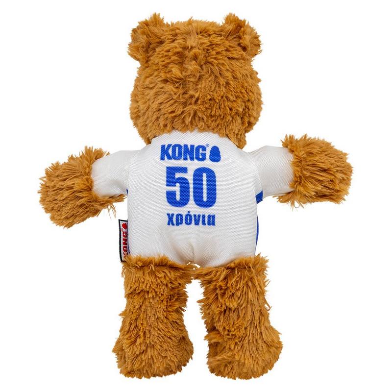 Ein flauschiger, brauner Teddybär steht mit dem Rücken zum Betrachter. Er trägt ein weißes T-Shirt mit blauen Ärmeln, darauf in Blau "KONG®", darunter eine große "50" und unten das Wort "χρόνια". Ein rotes KONG-Etikett hängt seitlich.