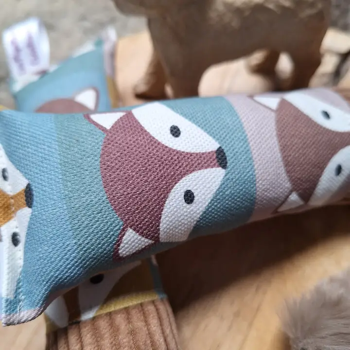 Ein Stoffspielzeug mit stilisierten Fuchsgesichtern in Pastellfarben auf einem Holzhintergrund.