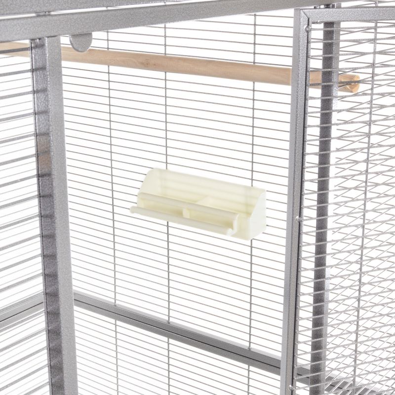 Interior view of a bird aviary with feeding bowl and perch in front of lattice wall.