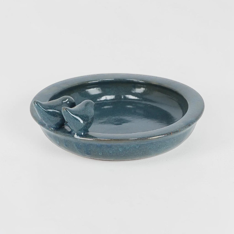 Abreuvoir rond en céramique bleu pétrole brillant, orné de deux petites figurines d'oiseaux stylisées sur le bord. Cuvette plate servant de point d'eau décoratif pour les oiseaux sauvages au jardin, terrasse ou balcon.