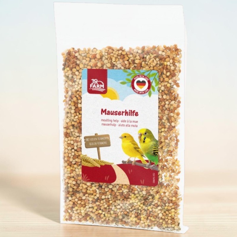 Sachet transparent de nourriture pour oiseaux avec graines diverses. Étiquette : « JR Farm Aide à la mue » avec canari jaune et perruche verte et jaune sur une branche. Panneau : « RICHE EN VITAMINES » sur ciel bleu avec soleil.