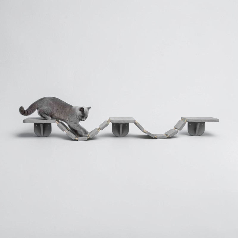 Un chat gris se tient en équilibre sur une échelle d'escalade de couleur taupe, à fixer au mur, en bois et sisal, posée contre un mur blanc. Il passe d'une plate-forme à un échelon souple pour rejoindre d'autres plates-formes. Longueur : 150 cm.