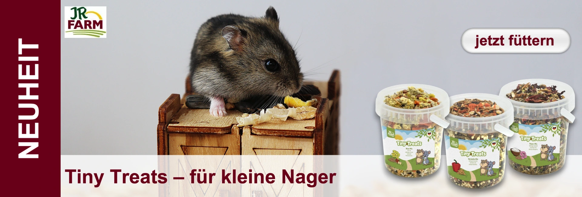 A hamster on a wooden box, next to it three transparent containers with food and a JR Farm logo.