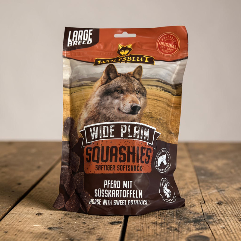 A standing, dark brown packet of ‘ Wolfsblut ’ Squashies dog treats for large breeds. The front features the head of a wolf in a vast grassy landscape and promotes ‘horse with sweet potatoes’ as the main ingredients for this juicy soft treat.
