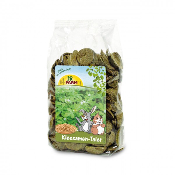 Transparent bag containing greenish, disc-shaped clover seed discs for animal feed. The label shows a brown rabbit, an orange and white guinea pig and a bowl of clover seeds. Brand: JR Farm, product name visible. For rodents and rabbits.
