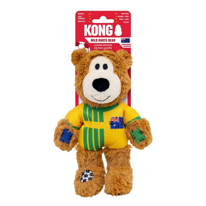 Ein brauner Plüschbär als Hundespielzeug von KONG steht aufrecht. Er trägt ein gelbes Trikot mit grünen Streifen und einem Patch der australischen Flagge auf der Brust. Blaue und grüne Flicken auf den Armen, Fußballmotiv am linken Fuß.