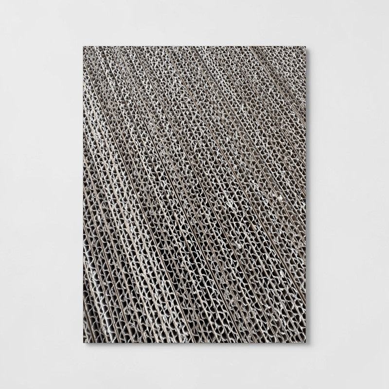 Close-up of stacked corrugated cardboard: the exposed edges reveal a pattern of corrugated lines and dark recesses. The numerous layers lie close together and run diagonally, creating an industrial texture.