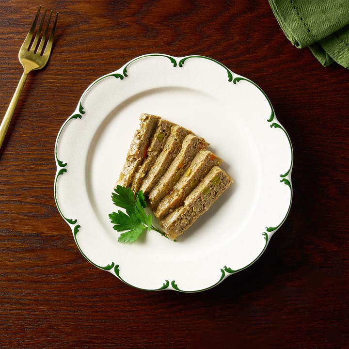 Portion rectangulaire de pâté pour chien à la dinde et au canard, garnie de persil, sur assiette blanche à bord vert. Morceaux de légumes et d’herbes visibles. Couverts dorés, serviette verte. Pâtée humide Canagan.