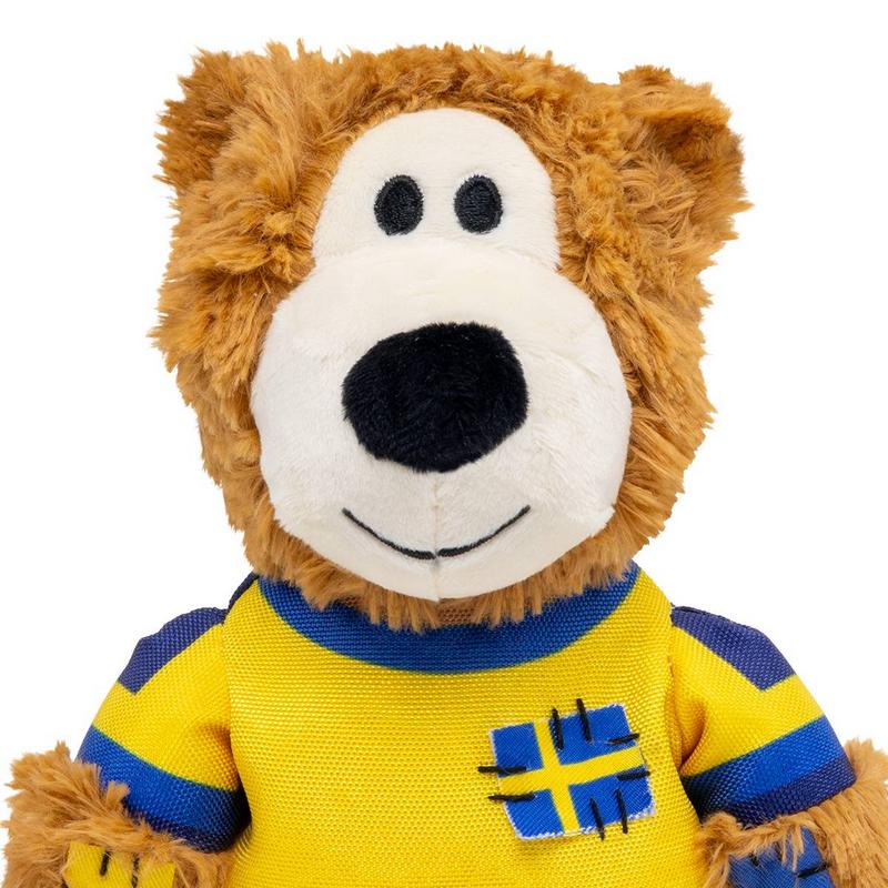 Orsacchiotto di peluche marrone con maglietta giallo-blu. Sul petto una toppa con la bandiera svedese. Muso bianco con grande naso nero, piccoli occhi neri e un sorriso amichevole ricamato. Pelliccia soffice, vestiti colorati.