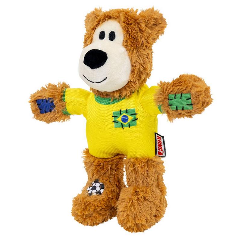 Morbido orsacchiotto marrone con espressione sorridente. Indossa una maglia da calcio gialla con colletto verde e bandiera brasiliana sul petto. Su zampe e piedi toppe ricamate, incluso motivo calcistico. Etichetta Kong rossa.