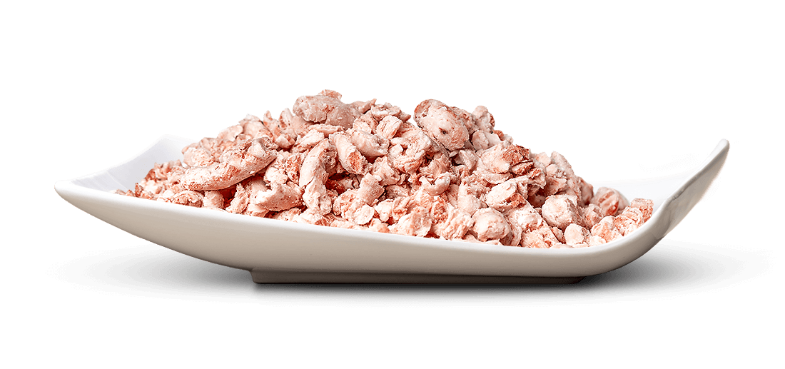 Ein weißes, schalenförmiges, blattähnliches Gefäß ist randvoll mit kleinen, unregelmäßig geformten Stücken getrockneter, rosafarbener oder hellbrauner Nahrung gefüllt. Die Stücke sind aufgehäuft und leicht pudrig.