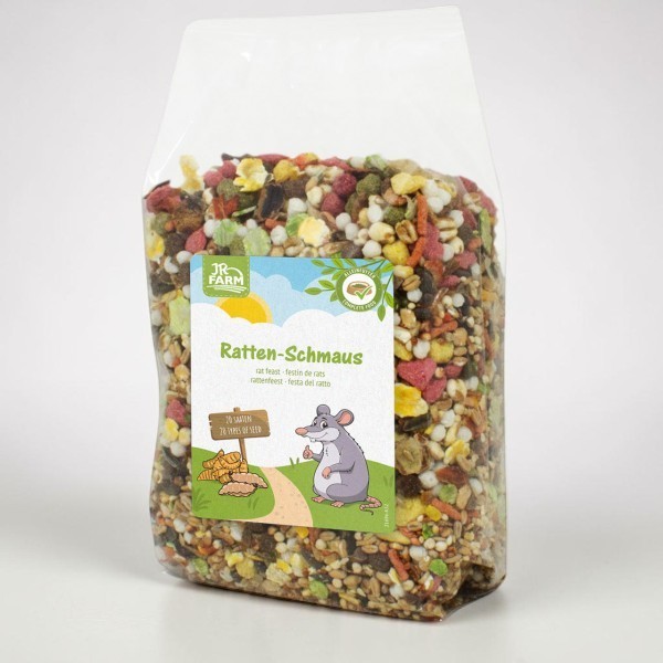 Sachet en plastique transparent contenant la nourriture pour rats « Ratten-Schmaus » JR Farm, mélange de graines colorées, granulés et fruits secs. Étiquette : rat de BD pouce levé, pancarte « 20 graines », soleil et prairies.