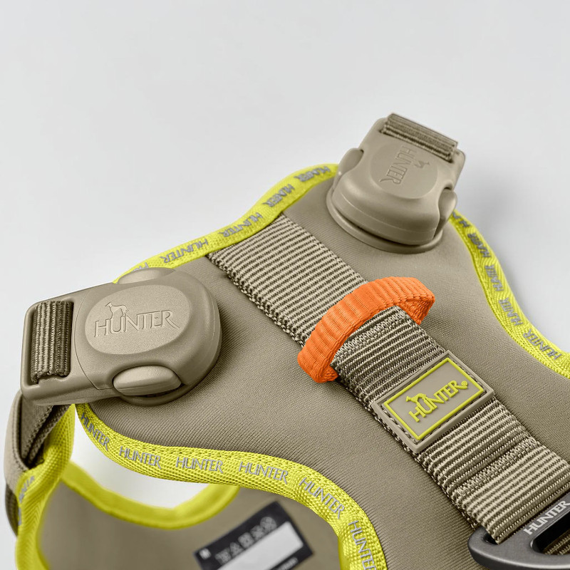 Ergonomic dog harness in grey-green with neon yellow piping and a reflective Hunter logo. Two magnetic buckles, wide strap, orange loop, Hunter label and aluminium D-ring.