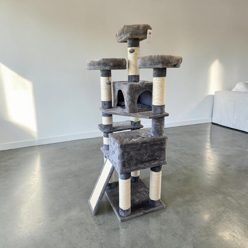 Ein großer, mehrstufiger Kratzbaum in Dunkelgrau und Beige steht auf Betonboden vor einer weißen Wand. Er hat mehrere Liegeflächen, zwei Höhlen, eine schräge Kratzrampe und viele sisalumwickelte Säulen.