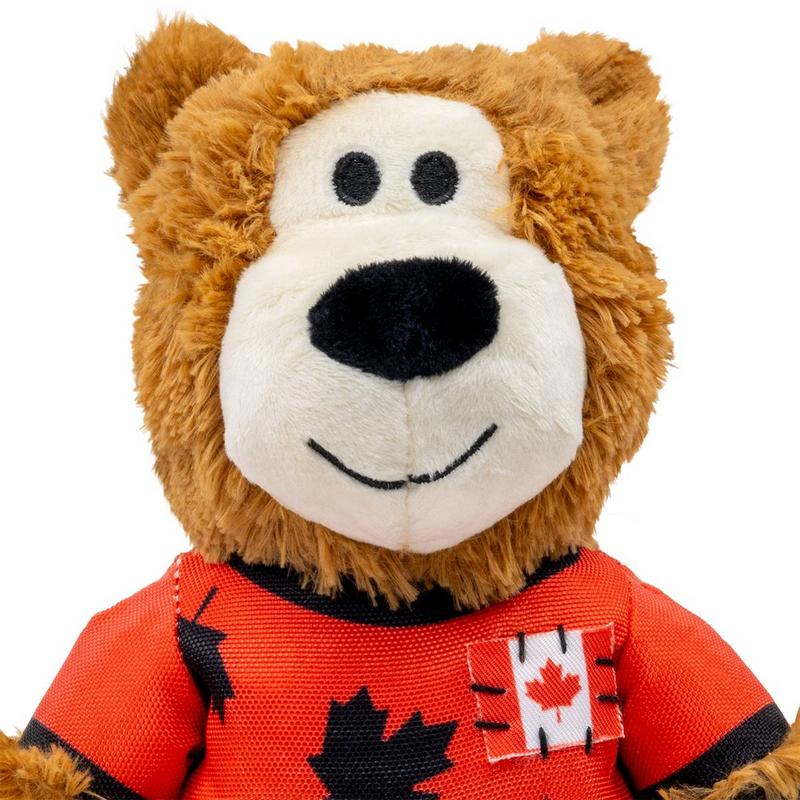 Flauschiger brauner Plüschbär mit hellbeigem Gesicht, runden schwarzen Knopfaugen und schwarzer ovaler Nase. Gesticktes Lächeln. Er trägt ein rotes T-Shirt mit schwarzen Ahornblättern und kanadischem Flaggen-Patch.