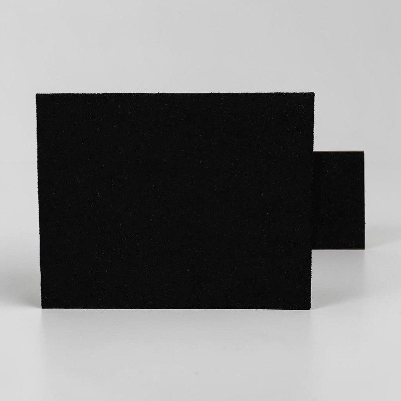 Une maison pour hérissons allongée en bitume noir à la surface rugueuse, vue de profil. Une partie plus petite et similaire dépasse sur le côté et forme l'entrée de l'abri. La texture est granuleuse et mate.