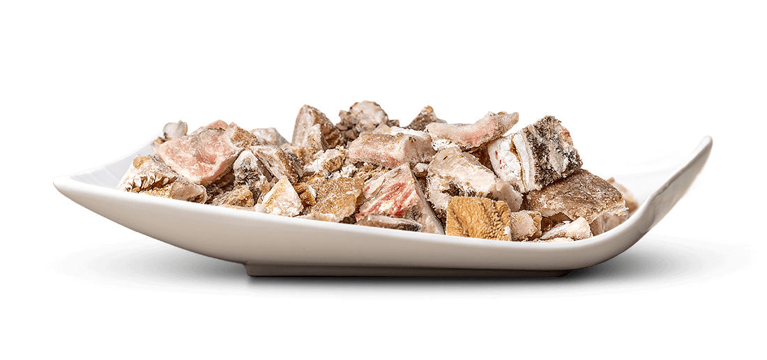 Eine weiße, längliche Schale, randvoll mit kleinen, unregelmäßig geformten Stücken gefrorenen Fleisches oder Innereien, liegt zentral auf weißem Hintergrund. Die Stücke sind rötlich, beige und braun und fein vereist.