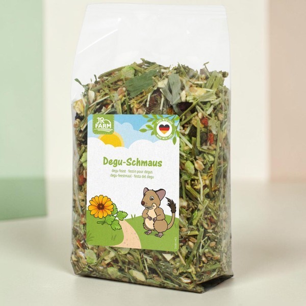 Sachet plastique transparent de nourriture pour dégus, mélange d'herbes séchées, graminées et graines. Étiquette « Degu-Schmaus », illustration d'un dégus avec fleur jaune sur herbe, logo JR Farm.