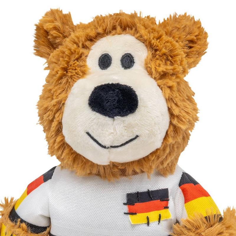 Un orsacchiotto di peluche dal pelo marrone e dall'espressione gentile. Indossa una maglia bianca con maniche nere, rosse e gialle e uno stemma con la bandiera tedesca sul petto. Si notano le morbide texture.