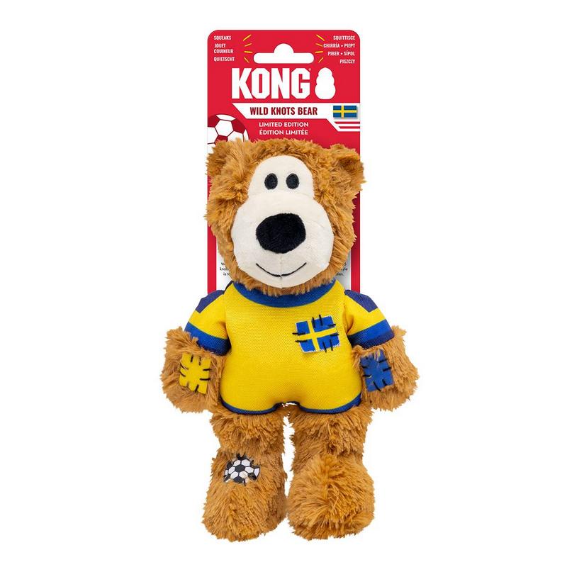 Un peluche a forma di orso per cani con pelo marrone, che indossa una maglia giallo-blu con la croce di Svezia stilizzata. Toppe blu sulle zampe, toppa con un pallone da calcio sulla gamba. Appeso davanti a una confezione rossa Kong.