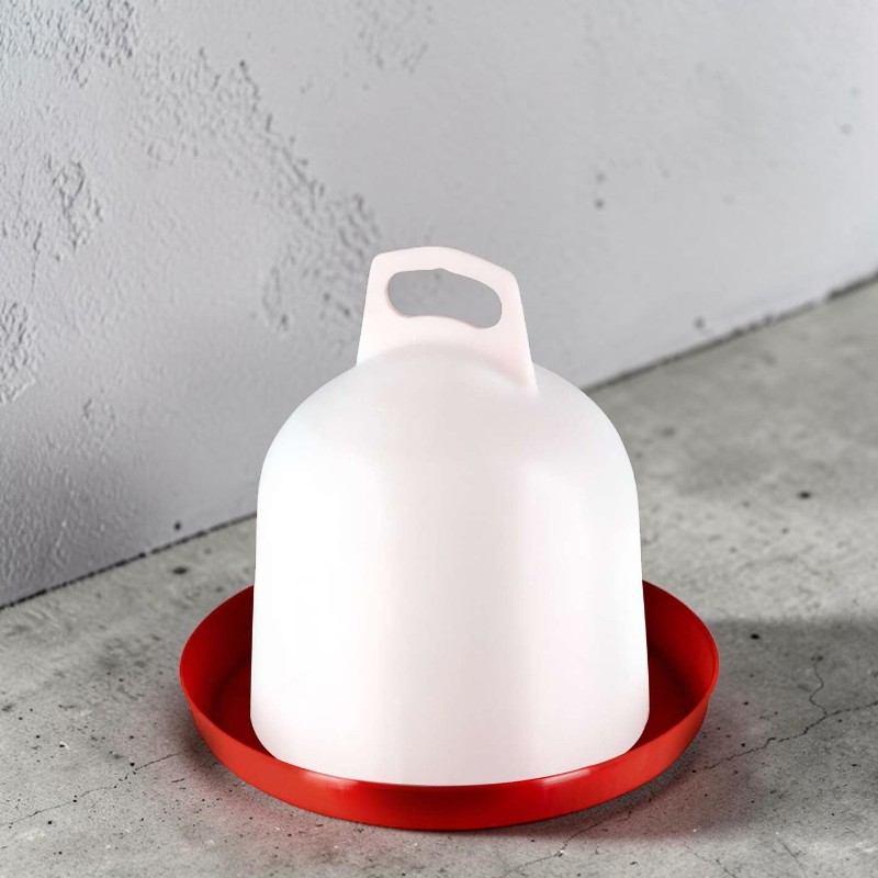 Weißer, glockenförmiger Kunststofftränker mit Griff oben, auf leuchtend roter, flacher Bodenschale. Steht auf grauem Betonboden vor strukturierter, hellgrauer Wand. Schatten im Hintergrund sichtbar.