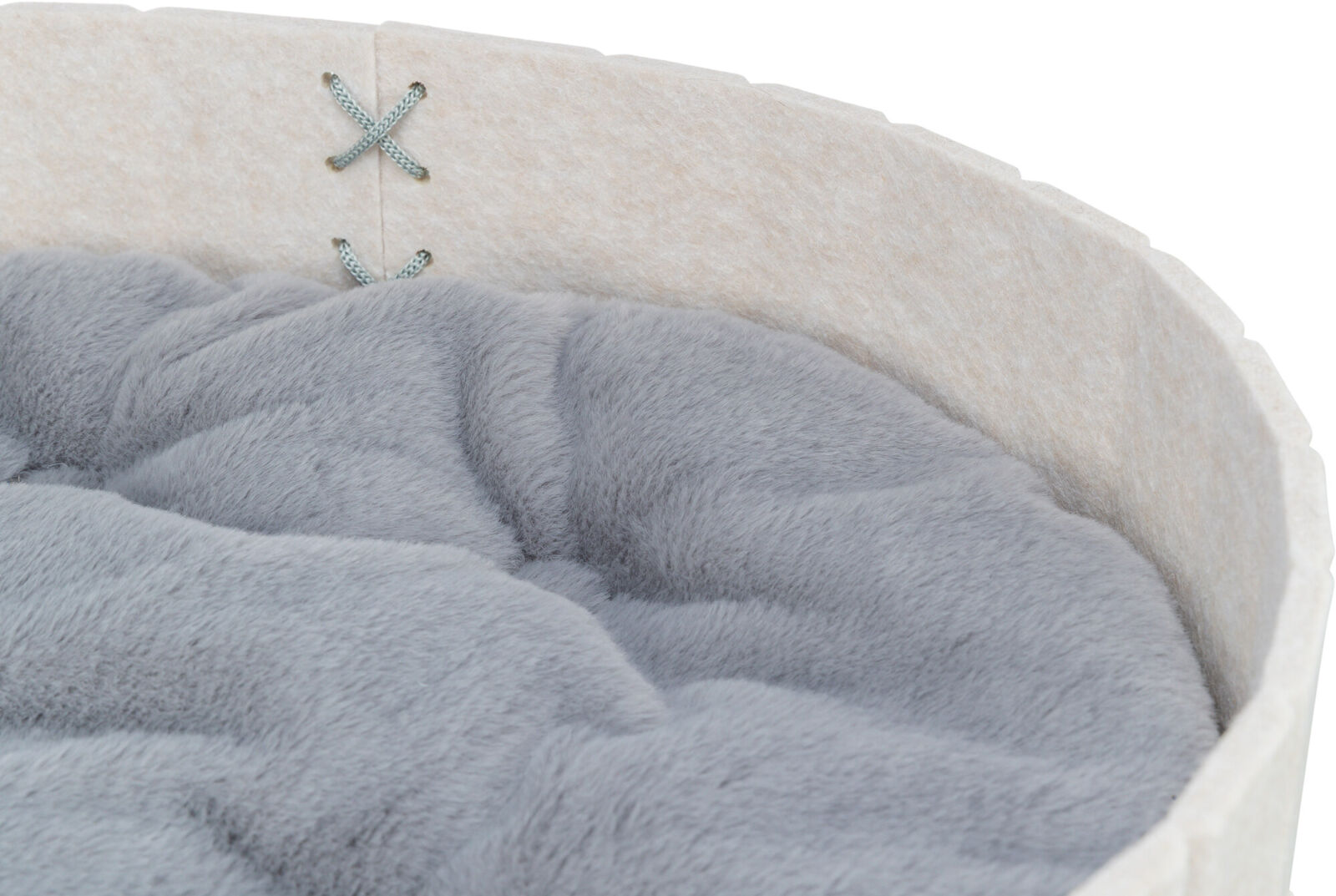 Primo piano di una cuccia rotonda per animali con rivestimento esterno color crema tipo feltro e morbido cuscino interno grigio chiaro. In alto due cuciture decorative a punto croce azzurre. Cuscino spesso e accogliente.