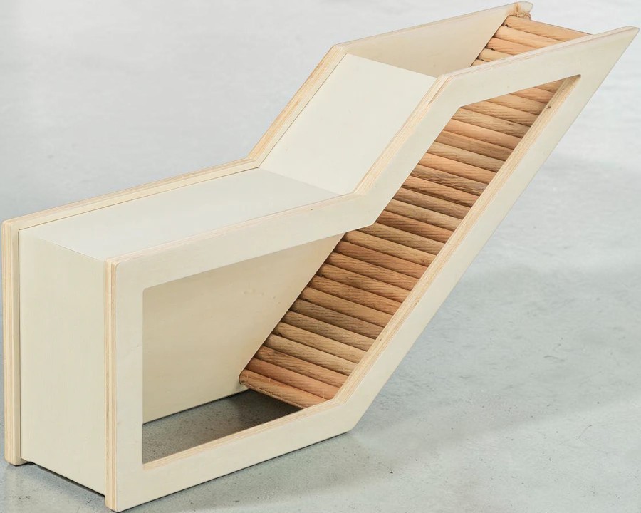 Rampa in legno beige chiaro per roditori con sezione superiore piatta e lato inclinato. La parte inclinata ha barre orizzontali in legno che creano una superficie scanalata come gradini/aiuto per arrampicarsi. Su base grigio chiaro.