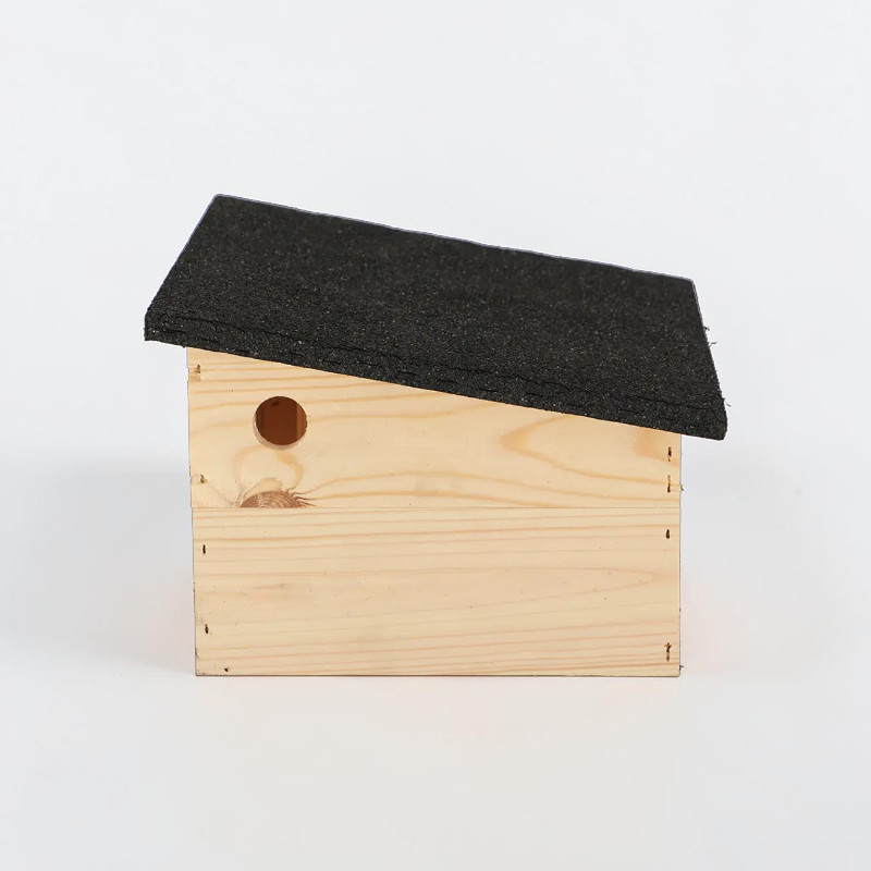Abri pour hérissons en bois d'épicéa clair non traité, doté d'un toit en bitume noir à pente inclinée, vu de face sur fond blanc. Ouverture d'entrée ronde à l'avant. Offre aux hérissons un refuge protégé pour se reposer et hiberner dans le jardin.