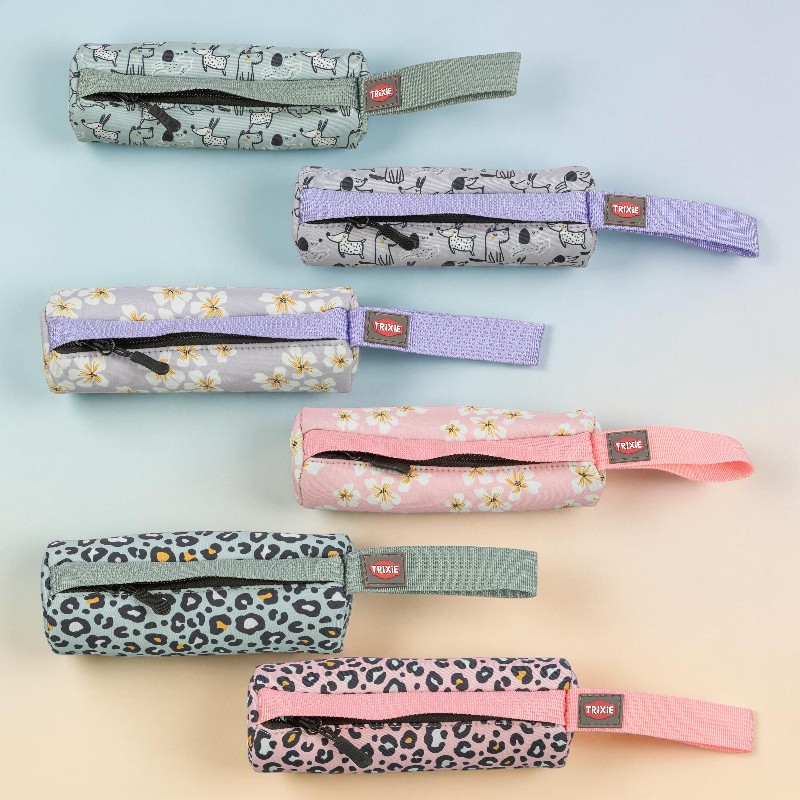 Sechs rechteckige Stofftaschen mit Reißverschluss und kleiner TRIXIE-Schlaufe sind horizontal auf Farbverlauf angeordnet. Designs: 2 mit Hunde-Motiven (grau, lila), 2 mit Blumenmustern (flieder, rosa), 2 mit Leopardenmuster (türkis, pink).