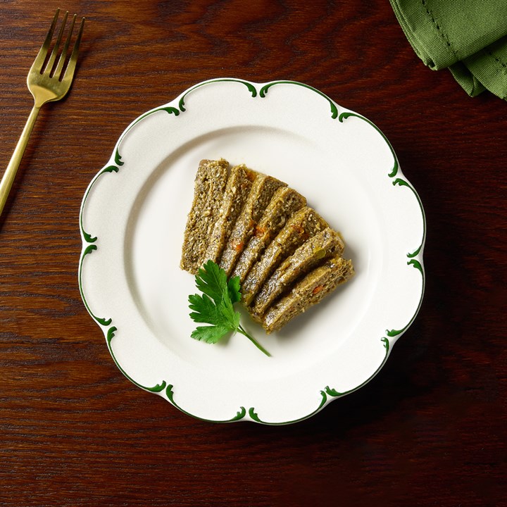 Pâté pour chien aux carottes et aux petits pois sur une assiette blanche, garni de persil ; à côté, une fourchette dorée, une serviette verte, une table en bois foncé.
