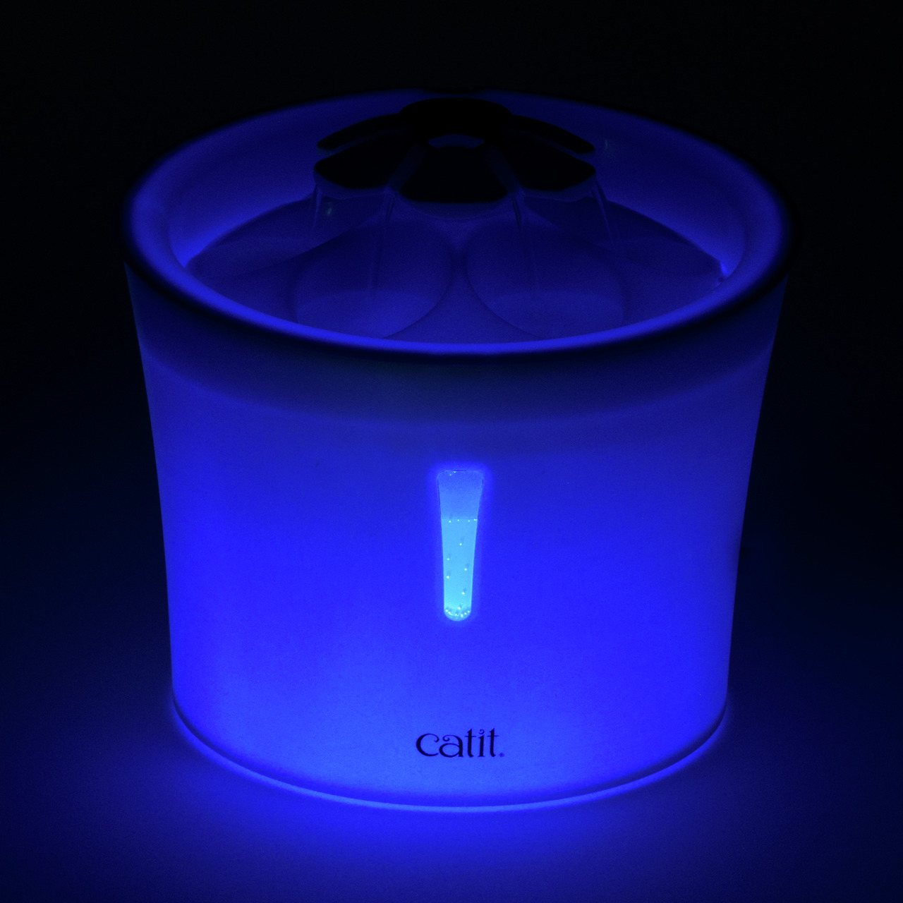 Leuchtender Catit LED-Trinkbrunnen Flower mit Wasserstandsanzeige im Dunkeln. Der Brunnen ist blau beleuchtet und hat einen Blütenaufsatz.