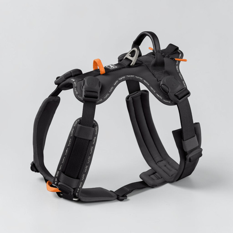 Black, ergonomic dog harness with wide, padded straps and orange accents. Adjustable straps, sturdy magnetic buckles and an aluminium D-ring on the back. Reflective Hunter lettering, Y-shaped chest pad.