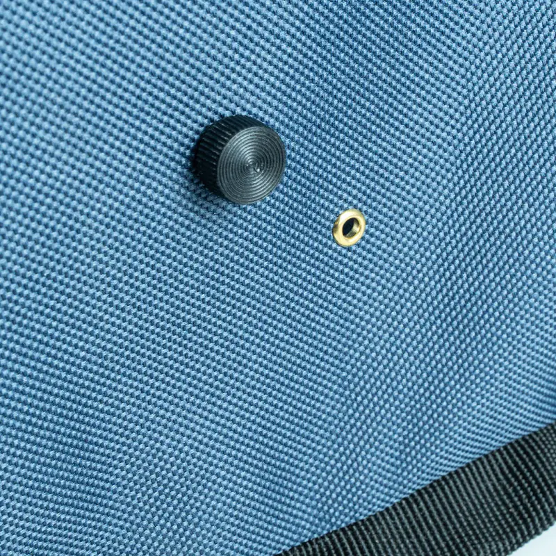 Close-up of a blue bag with knob and eyelet. The material looks like a robust fabric.
