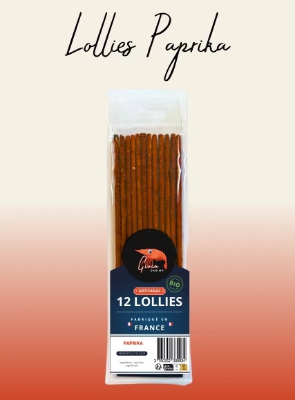 Confezione trasparente con 12 lecca-lecca al peperone rosso-marrone. Bastoncini artigianali con etichetta nera: Gioia logo SHRIMP, bio, origine Francia e codice a barre. In alto "Lecca-lecca al peperone" in corsivo beige-arancione.