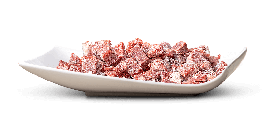 Eine flache, weiße, rechteckige Schale mit sanft geschwungenen Seitenrändern ist gefüllt mit vielen kleinen, unregelmäßigen Stücken dunkelroter Früchte, kandiert oder getrocknet, leicht von einer feinen Zuckerschicht bedeckt.
