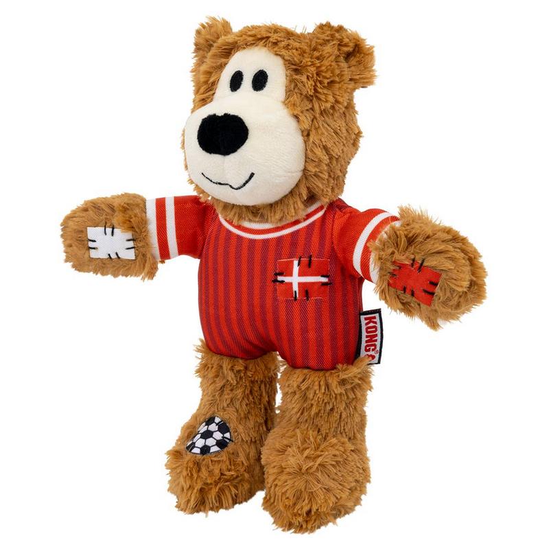 Orsacchiotto di peluche marrone con pancia bianca e naso nero. Indossa maglia a strisce rosse e bianche con croce bianca sul petto e toppe bianche su braccia e piedi. Toppa sul piede: motivo calcistico; etichetta Kong.