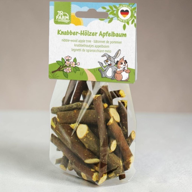 Transparent plastic packaging containing short, natural apple tree chew sticks for small animals. Coloured label bearing the title ‘Apple Tree Chew Sticks’, the JR Farm logo, blossoming branches and two rodent figures in a meadow.