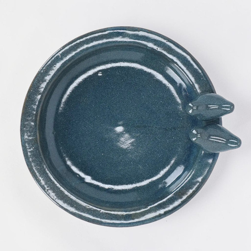Abreuvoir rond en céramique couleur pétrole, vu d'en haut. Cuvette brillante à la surface mouchetée, rebord surélevé rehaussé de touches claires. Deux petits oiseaux stylisés sur le bord sup. droit.