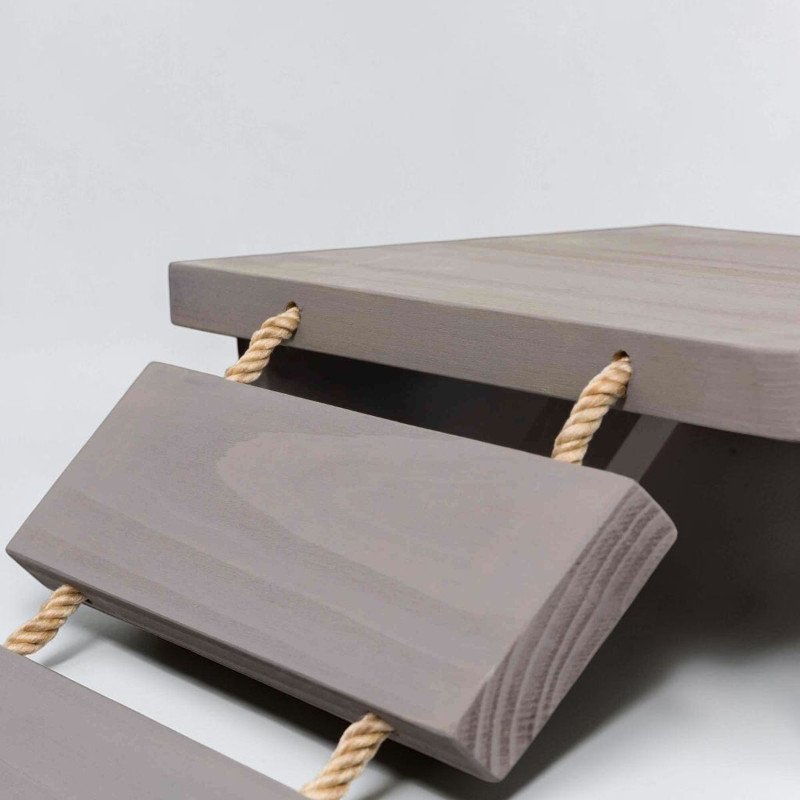 Gros plan sur une échelle d'escalade en bois taupe à fixer au mur. Les échelons rectangulaires sont reliés par d'épaisses cordes en sisal beige, passées dans des trous. En haut, une plate-forme, et dessous, deux échelons inclinés.
